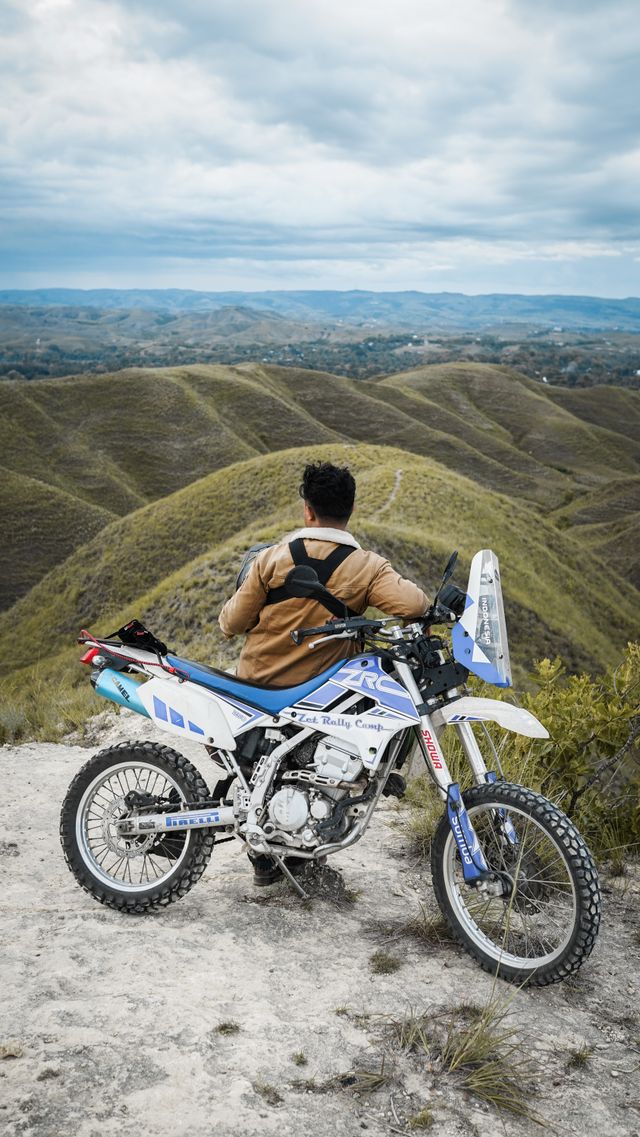 A rider pausing on a motorcycle overlooking rolling green hills