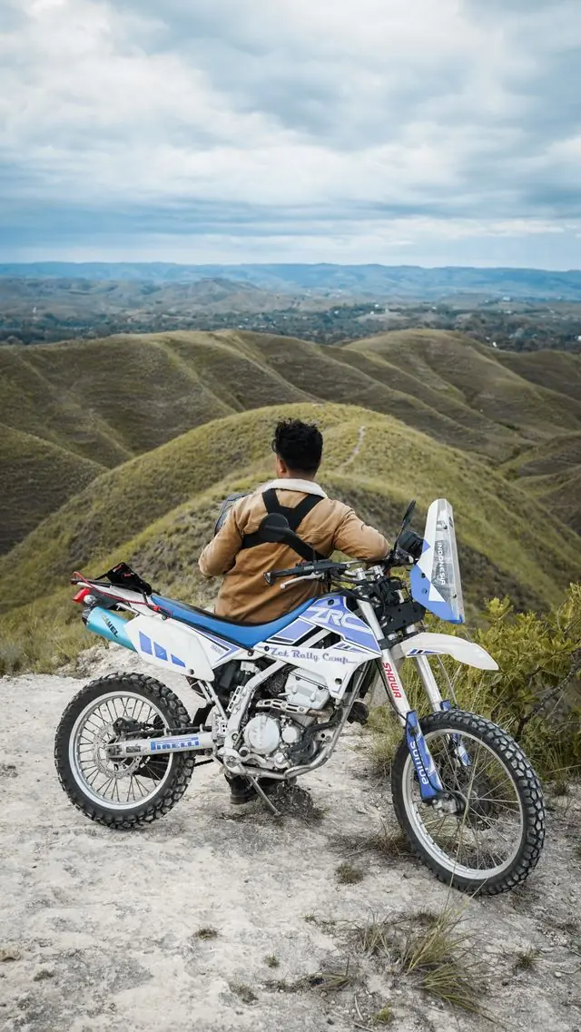 A rider pausing on a motorcycle overlooking rolling green hills