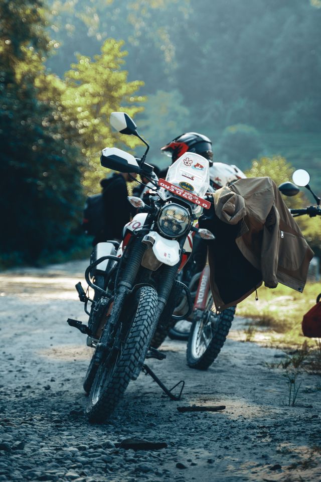 A rider pausing on a misty unsurfaced mountain road with other motorcycles nearby