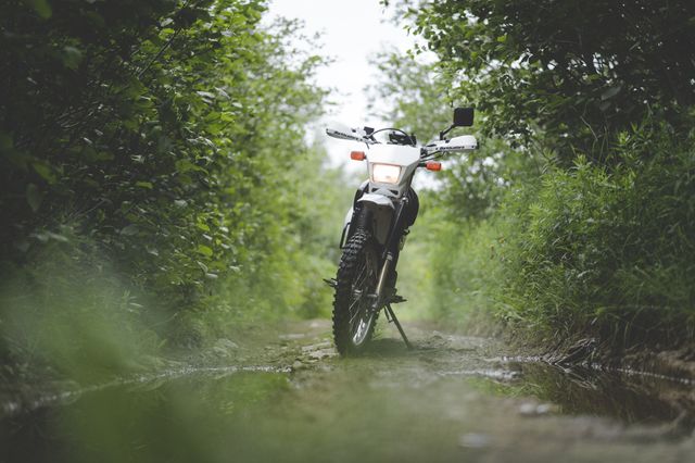 A trail motorcycle stopped on a green, hedge-lined unsurfaced lane