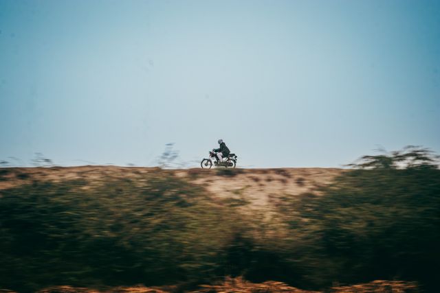 A motorcycle rider crossing an open grassy hilltop in motion