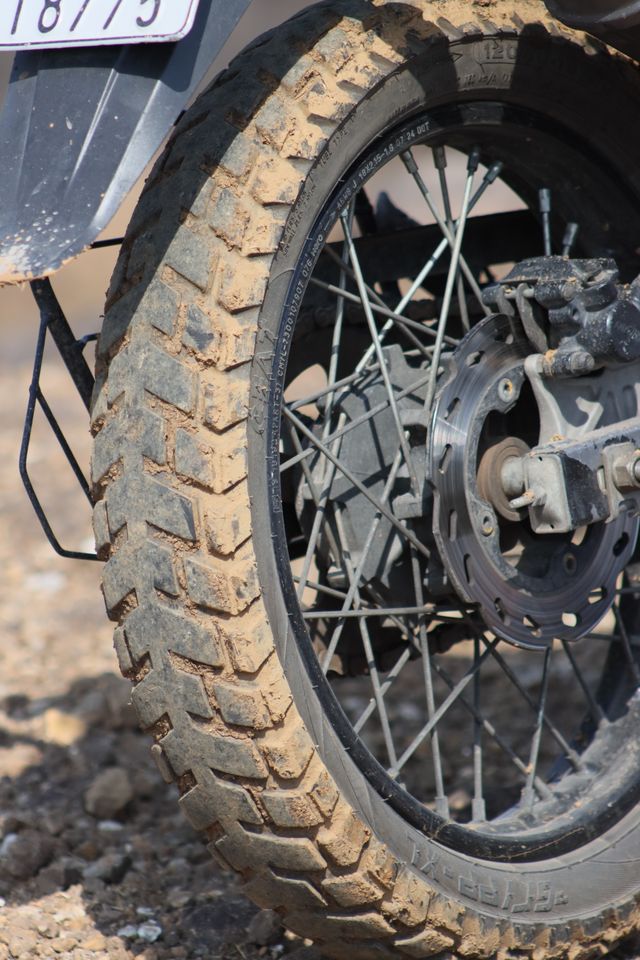 A close-up of a muddy motorcycle tyre and rear disc brake