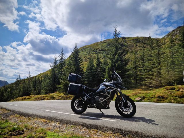 An adventure motorcycle parked on a road beside a forested hillside