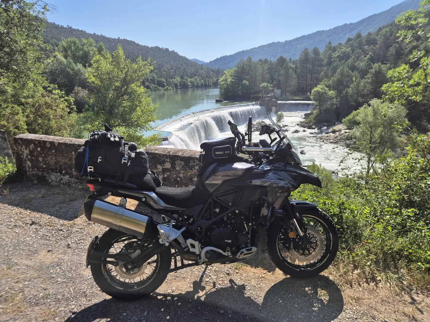 Benelli TRK 502X parked above a weir on a river in the French Pyrenees, fully loaded with touring luggage