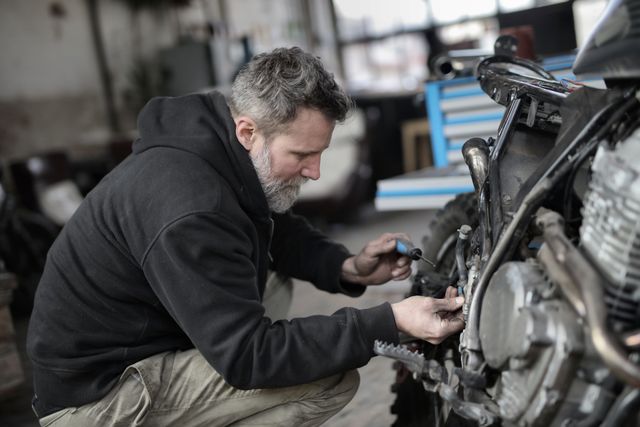 A person servicing a motorcycle's chain and sprocket in a garage