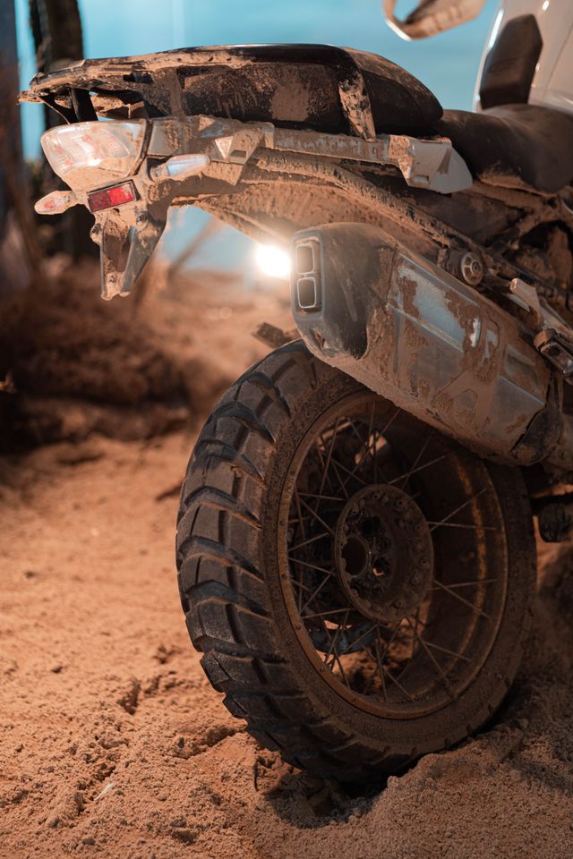 A heavily mud-caked adventure bike's rear end, exhaust and mudguard caked in dried clay