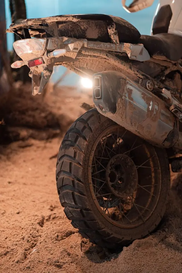 A heavily mud-caked adventure bike's rear end, exhaust and mudguard caked in dried clay
