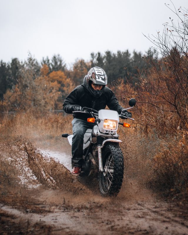 A rider crossing a muddy, waterlogged trail on a trail bike, throwing up spray