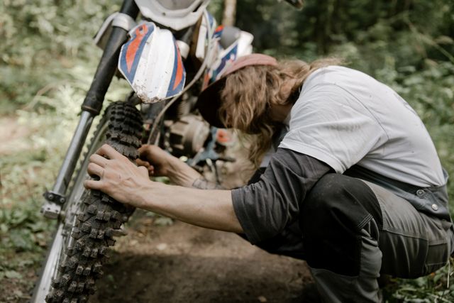 A rider inspecting a motorcycle's front tyre and forks on a trail