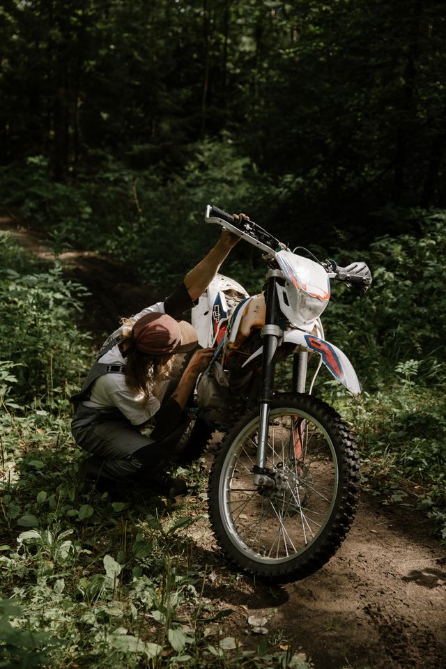 A rider adjusting the handlebar controls on a dirt bike in the woods