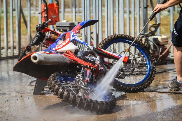 A person pressure washing a muddy trail bike
