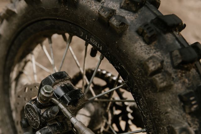 A close-up of a muddy spoked wheel and brake calliper