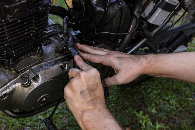 A pair of hands checking wiring and connectors on a motorcycle engine