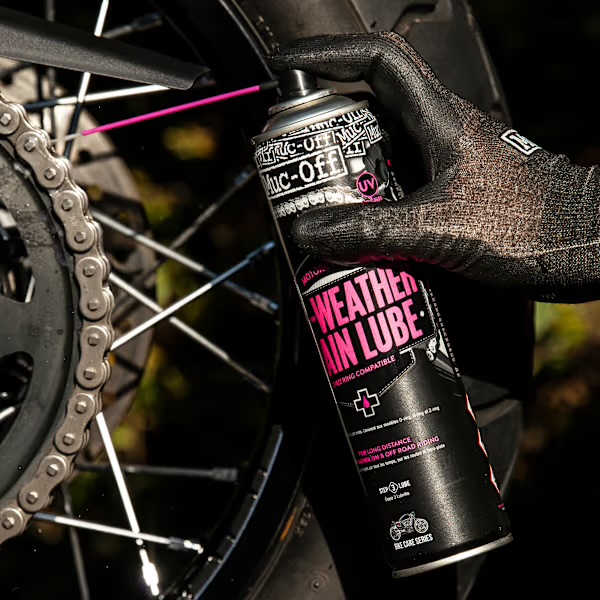 Muc-Off All-Weather Chain Lube being sprayed onto a muddy trail bike chain