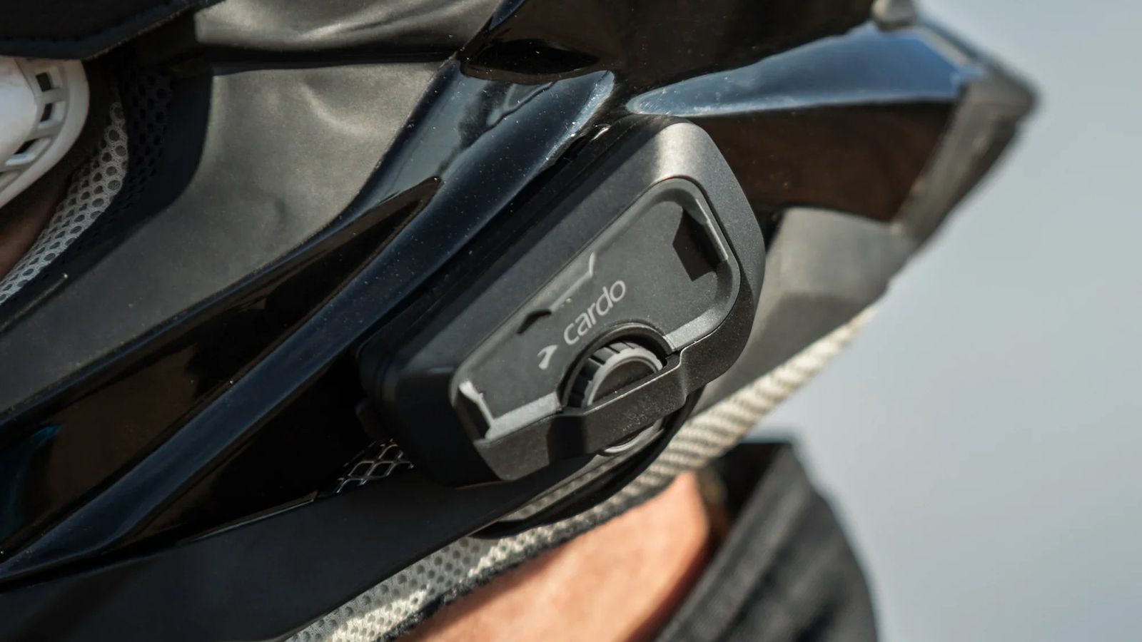 A Cardo intercom clamped to the side of a peaked adventure helmet