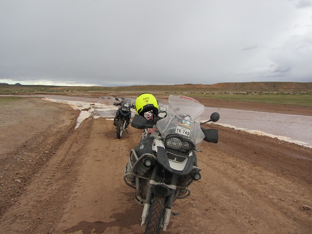 two adventure motorcycles stopped beside a flooded track under an overcast sky