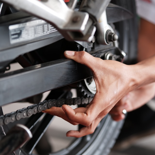 a rider's hand checking motorcycle chain tension and lubrication
