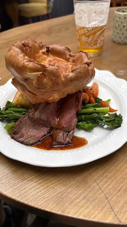 A roast beef dinner with a large Yorkshire pudding and greens, with a pint behind it, at the New Sun Inn in Kimbolton